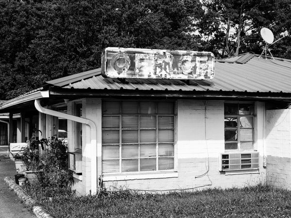 Black and white photograph of a faded and peeling vintage neon motel office sign on a motel that's still open for business in the southern city of Columbus, Georgia.