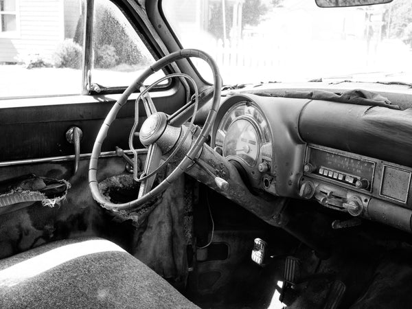 Black and white photograph of the ripped and dusty interior of a rusty antique car shot with a high-resolution medium format camera.