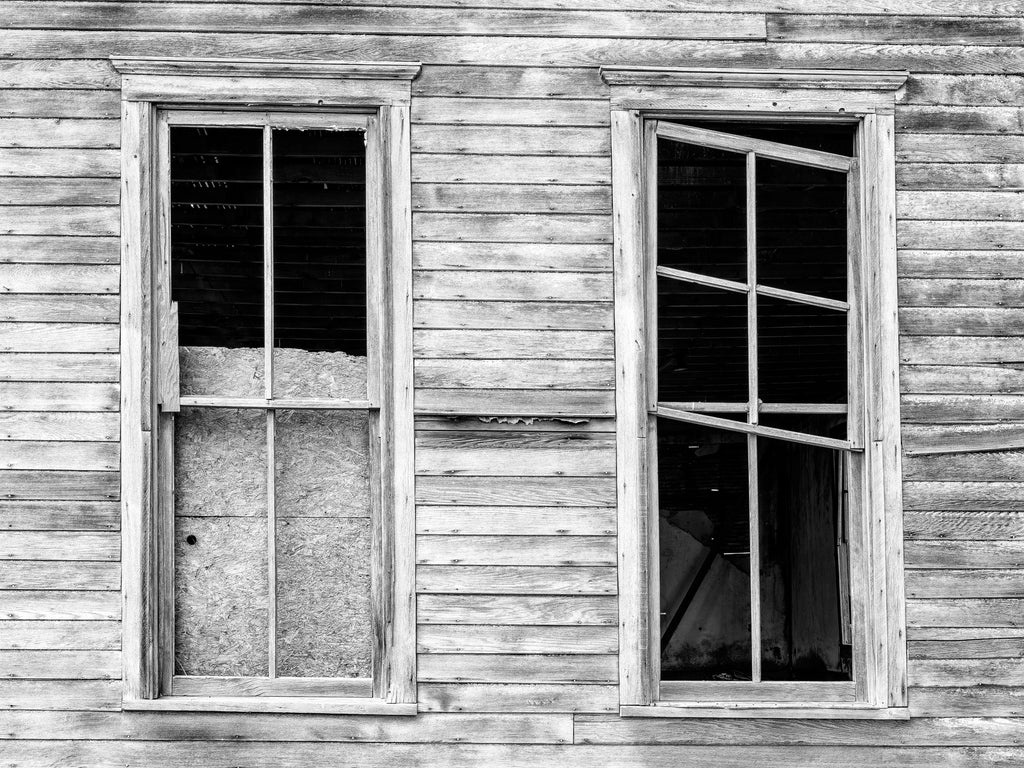 Black and white photograph of the broken windows of an abandoned wooden church in the almost-a-ghost-town at Cottonwood on the prairie of South Dakota. 