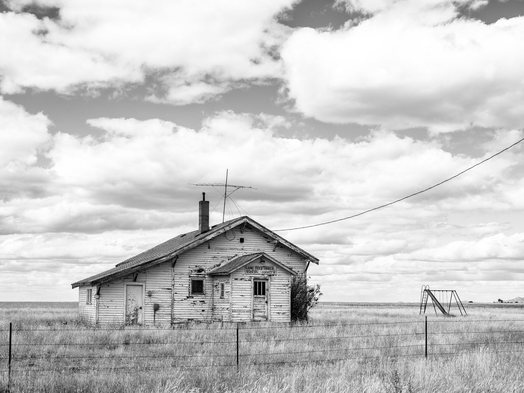 Black and white photograph of the abandoned Lone Tree Bench School standing on the rugged rolling prairie of Montana.