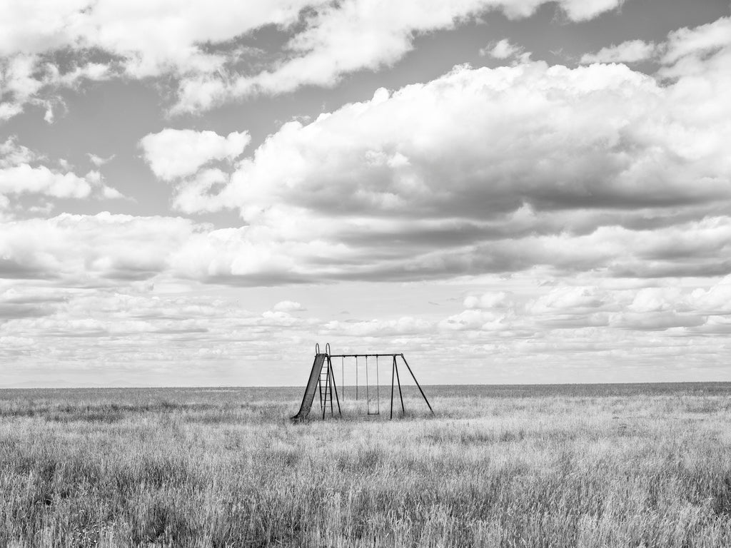 Black and white photograph of what may be the loneliest abandoned school playground in America, found on the rugged rolling prairie of Montana.