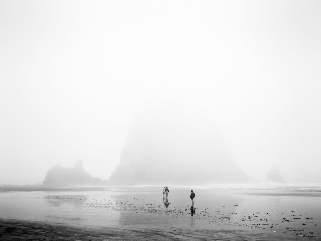 Black and white photograph of Oregon's iconic coastal landmark, Haystack Rock, cloaked in a dense layer of morning fog.