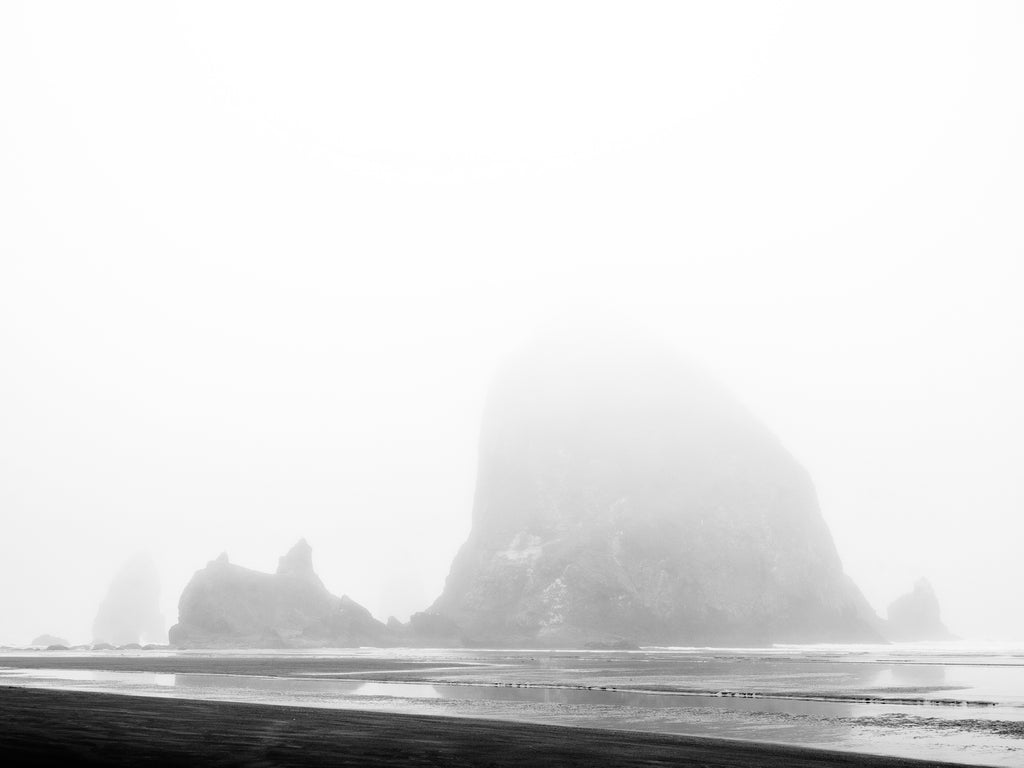 Black and white photograph of Oregon's Haystack Rock, an iconic coastal landmark in Cannon Beach, cloaked in a layer of dense morning fog.