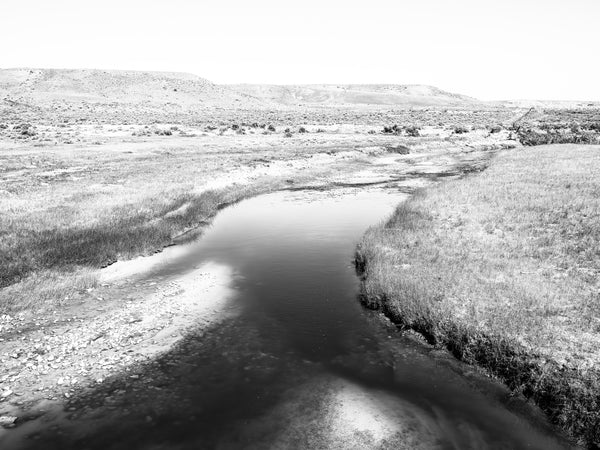 Black and white photograph of shallow creek winding through the vast and rugged Wyoming landscape near the location of historic Fort Bridger.