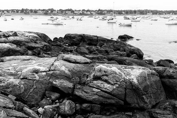 Black and white photograph of sail boats anchored in a placid, rocky harbor along the coast of New England.