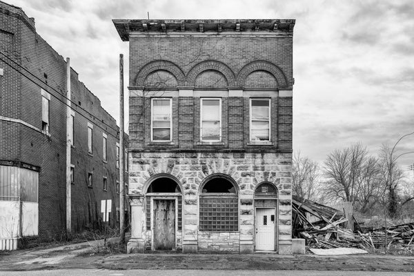 Black and white photograph of an abandoned building on a city block of derelict or demolished buildings in Mounds, Illinois.