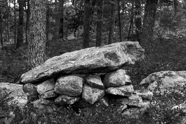Black and white photograph of an old stacked stone wall found in the green forest of New Hampshire.