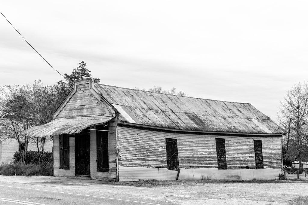 Black and white photograph of a leaning old wooden store building with a tin roof now standing abandoned in the small rural community of Newbern, Alabama.