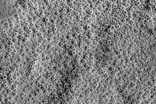 Black and white photograph of tiny air bubbles under the surface of the water alongside the shallow edges of a stream.