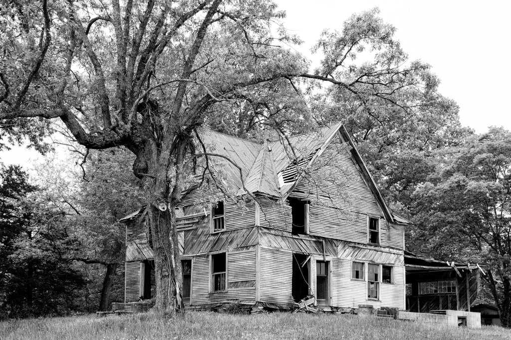 Black and white photograph of the ruins of a big abandoned house on the top of a hill.