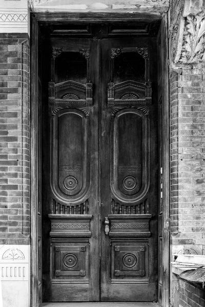 Black and white detail photograph of the beautiful ornate wooden double-doors on the front of a Victorian mansion.