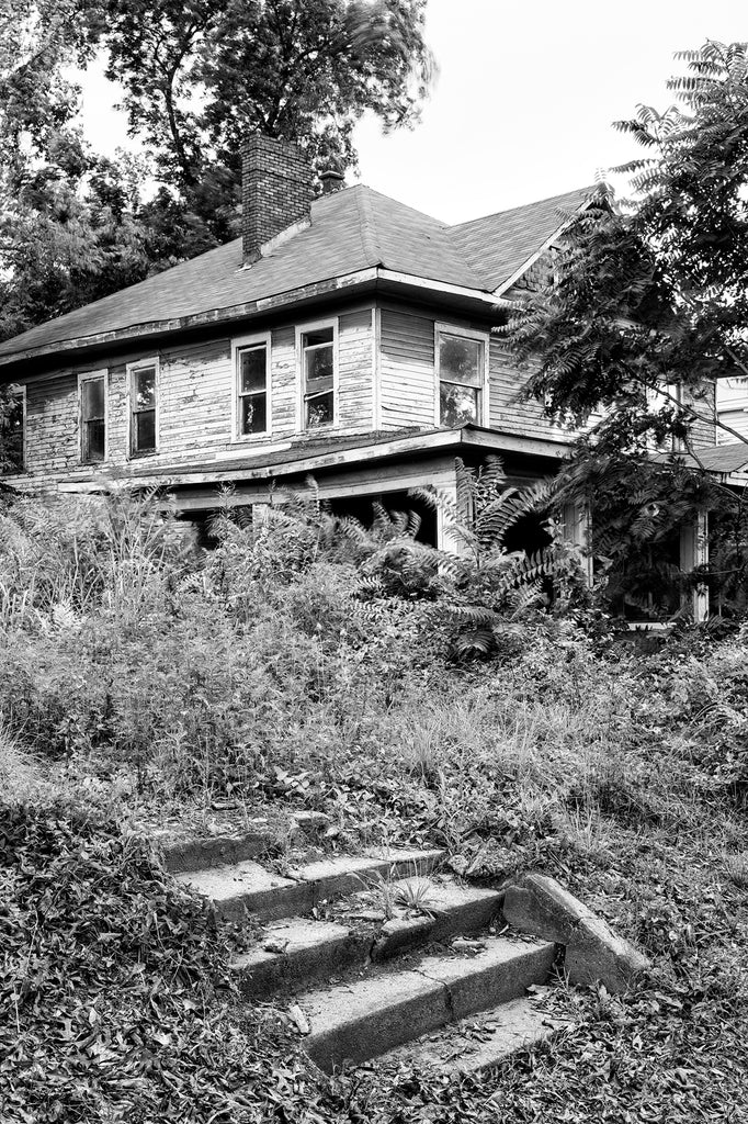 Black and white photograph of an abandoned house in the historic Norwood neighborhood of Birmingham, Alabama, where occupied mansions sit next door to vacant lots or derelict ruins of old houses.