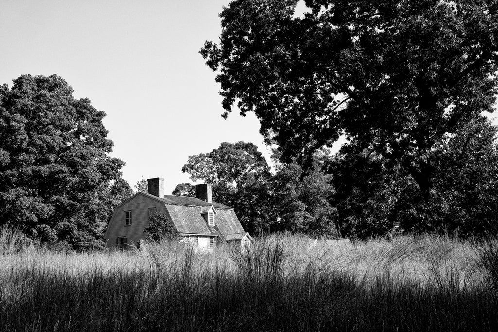Black and white photograph of the historic landscape at Concord, Massachusetts with a beautiful historic home tucked away among tall grass and towering trees.