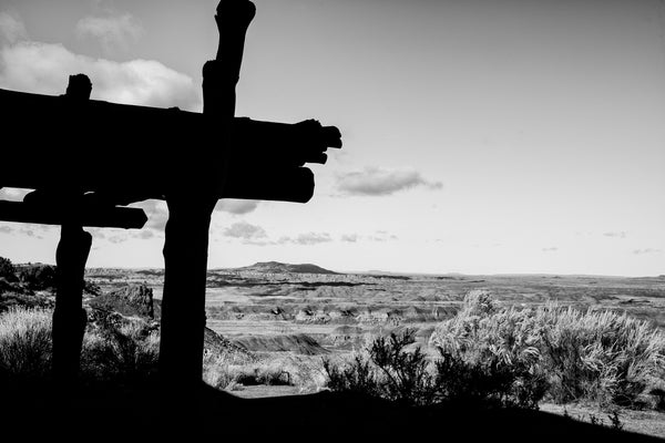 Black and white photograph of the vast Arizona landscape at the Painted Desert with rustic porch columns of the Painted Desert Inn silhouetted in the foreground.