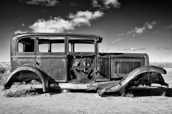 Black and white photograph of a rusty 1932 Studebaker displayed in the Petrified Forest National Park to mark an alignment of Route 66 that once ran through the park.