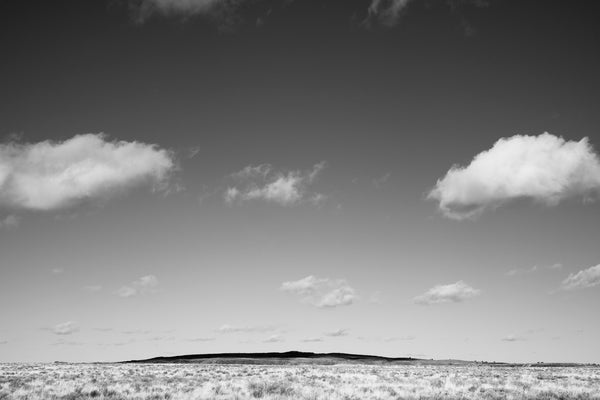 Black and white photograph of the vast Arizona landscape with puffy white clouds casting shadows over a distant mountain range.