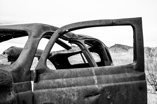 Black and white photograph of a rusty old car parked at Cool Springs Service Station on Route 66 with a view of the rugged Arizona mountains.