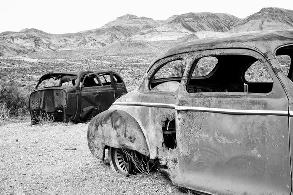Black and white photograph of rusty old cars sitting at Cool Springs Service Station on Route 66 in the rugged Arizona mountains.