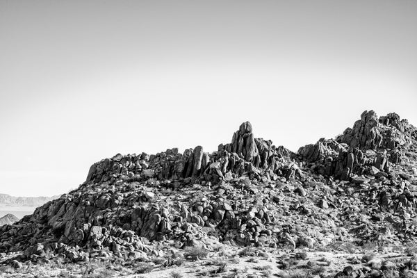 Black and white landscape photograph of a boulder-strewn ridge line in the California desert at Joshua Tree National Park.