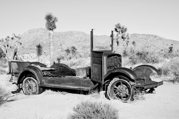 Black and white landscape photograph featuring the rusty remains of an abandoned truck left decades ago in the desert at California's Joshua Tree National Park.