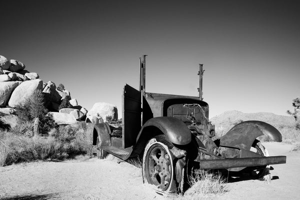 Black and white landscape photograph with the skeletal remains of a rusty old truck sitting abandoned in the desert of Joshua Tree National Park in California.