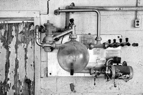 Black and white photograph of an old milk pump in the milking parlor of a former dairy farm.