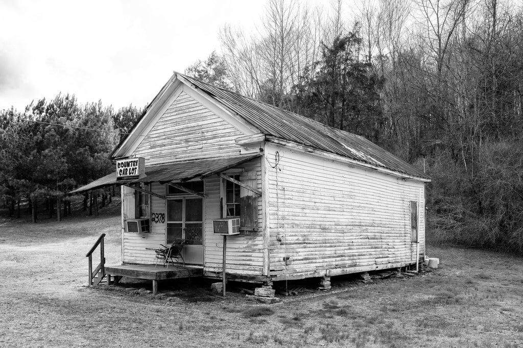 Black and white photograph of an abandoned old general store building that ended its useful existence as a used car lot along a back road in the rural American South.
