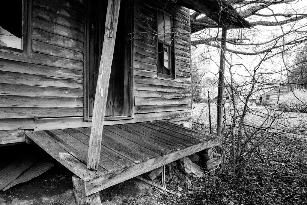 Black and white photograph of the sloping front porch of an abandoned old wooden country store in rural Tennessee near Lynchburg.