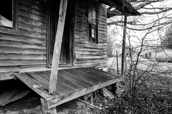 Black and white photograph of the sloping front porch of an abandoned old wooden country store in rural Tennessee near Lynchburg.