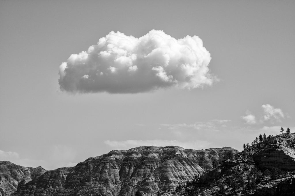 Black and white photograph of a puffy white cloud floating over the rugged Montana mountain landscape at the Missouri Breaks.