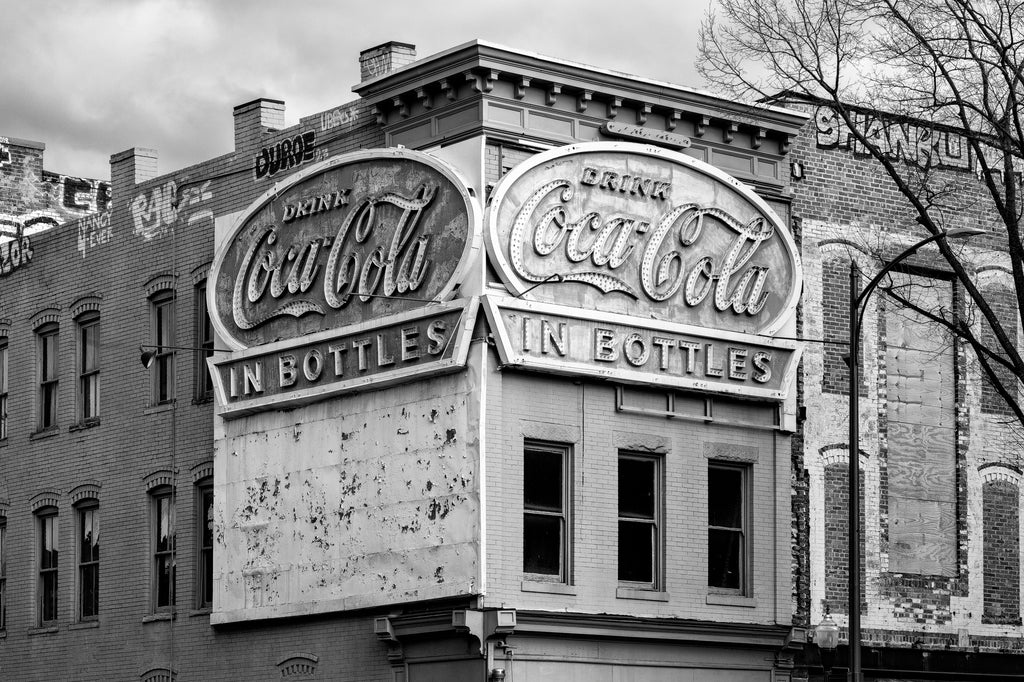 Black and white photograph of a historic brick building corner on Broad Steet in Richmond featuring large vintage Coca-Cola 'In Bottles' signs mounted on the exterior walls.