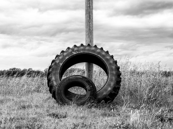 Black and white photograph of two tires, one large tire and one small, leaned against a utility pole in the grass along Highway 61 in the Mississippi Delta farm landscape near Shelby.