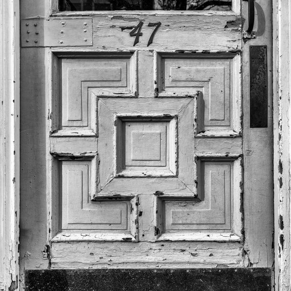 Black and white photograph of the rectangular designs of an old door on a storefront in a small New England town. (Square format)