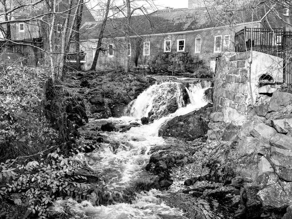 Black and white photograph of a small cascade over large rocks in the Powwow River near an old mill site in Amesbury, Massachusetts.