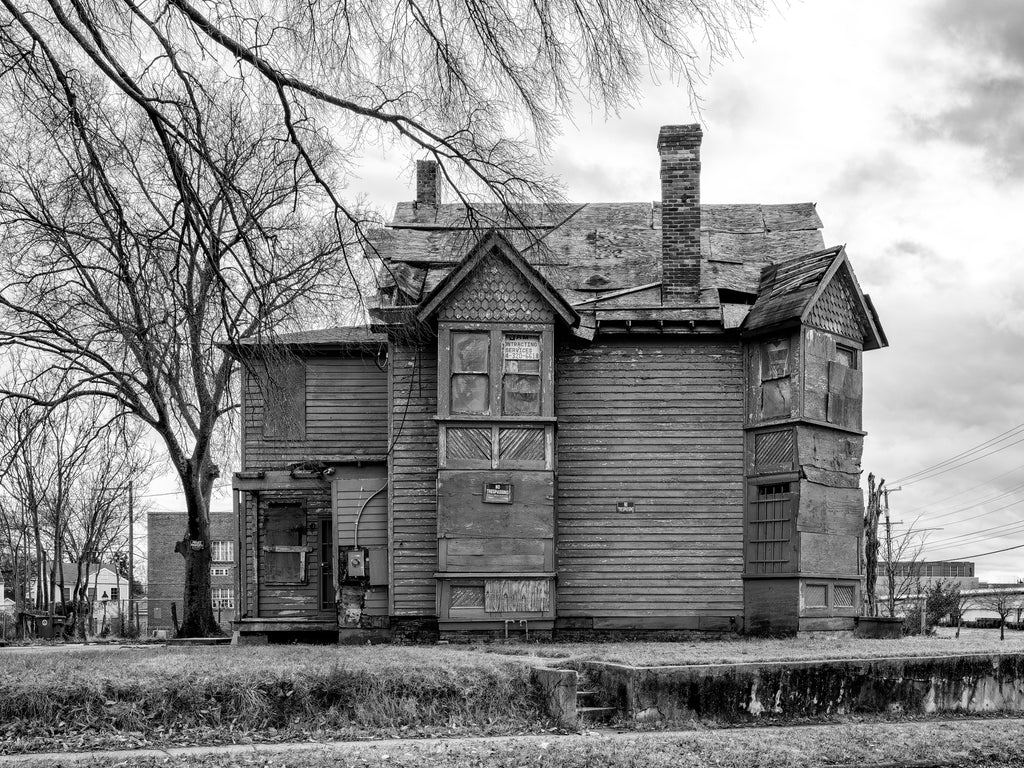 Black and white photograph of a formerly magnificent house now standing boarded-up and abandoned on a corner lot in Richmond, Virginia.
