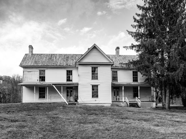 Black and white photograph of a beautiful two-story white farmhouse standing vacant along historic Route 11 in rural Virginia.
