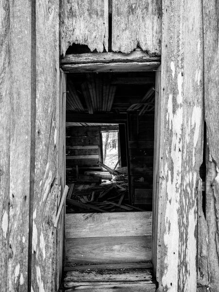 Black and white photograph of an open window framed by weathered wooden planks on the exterior of an abandoned 1920s farmhouse built by Eli Tillman in the rural American South.