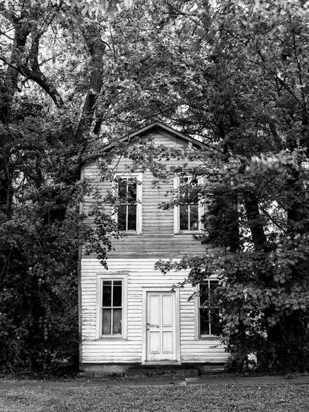 Black and white photograph of a large two-story abandoned house peeking out from behind tree branches in the beautiful small town of Bardstown, Kentucky