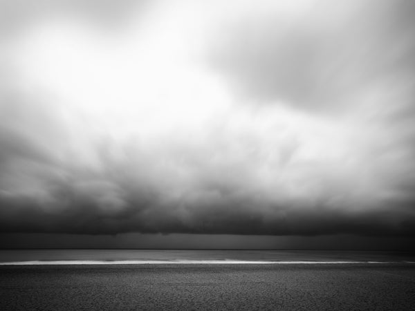 Black and white long-exposure photograph of dark, heavy storm clouds hanging low over the Atlantic Ocean along the New England coast.