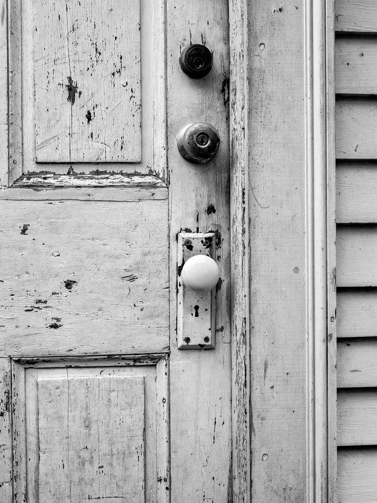 Black and white photograph of the grimy and weathered front door of an old white house in New England.