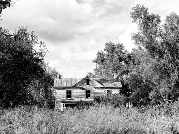Black and white photograph of a beautiful two-story wooden farmhouse standing amid tall grass and trees in rural Virginia in the American South.