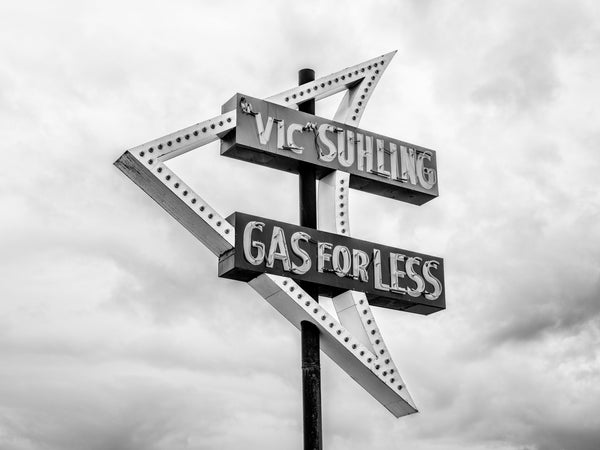 Black and white photograph of a classic Route 66 neon sign that says "Vic Suhling Gas for Less." The sign was erected in 1957 for a gas station along the Mother Road in Litchfield, Illinois. Suhling's gas station closed in 1968; the building was demolished in 1990, and the sign still stands in its original location over the site of a museum and Route 66 welcome center.