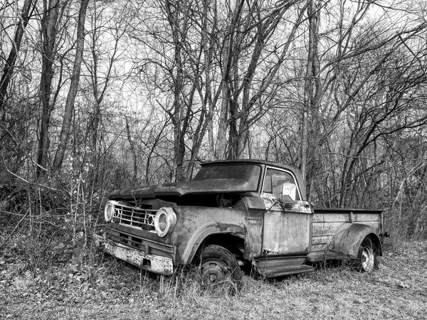 Black and white photograph of an abandoned old Dodge 300 work truck found in the grass alongside a rural country road.