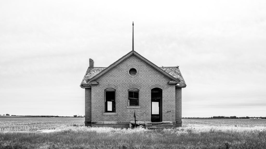 Black and white photograph of an abandoned one-room schoolhouse built 1920 on the broad prairie of Kansas, shot in wide 16 x 9 panoramic format.