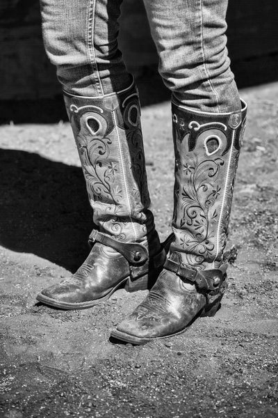 Black and white photograph of tall ornately stitched western boots on a female rodeo rider.