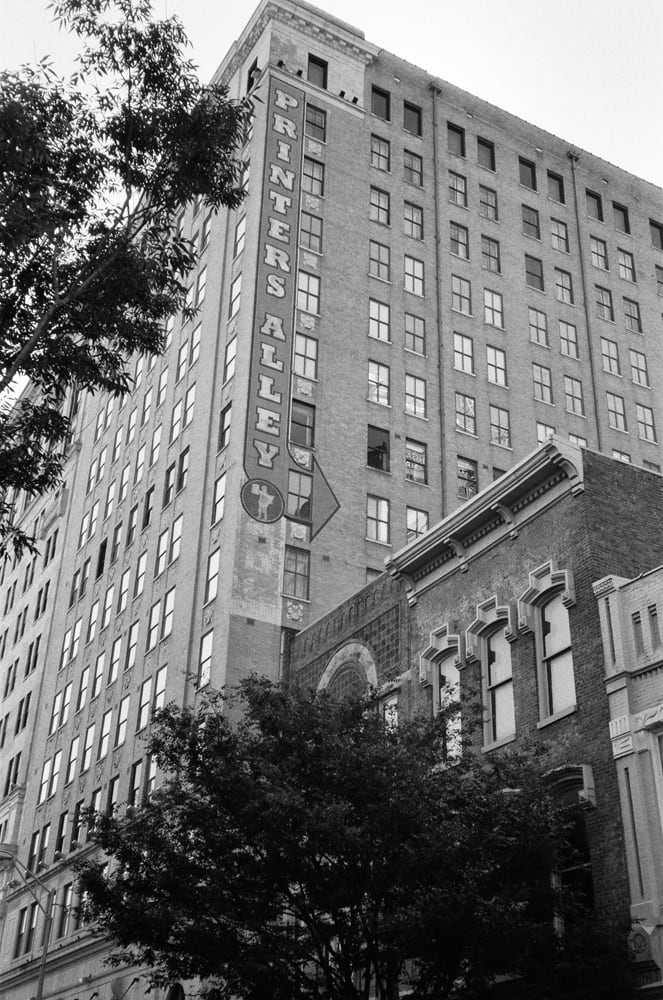Black and white photograph of a tall Printer's Alley sign painted onto the sign of a building in Nashville. 