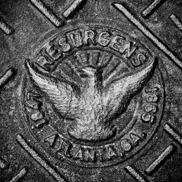 Black and white photograph Atlanta's Resurgens phoenix icon casy into a heavy iron man hole cover.