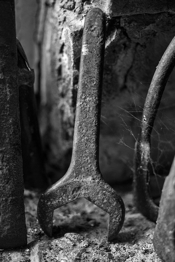 Black and white photograph of a rusty old wrench, clung with cobwebs, found in the basement of an old house.