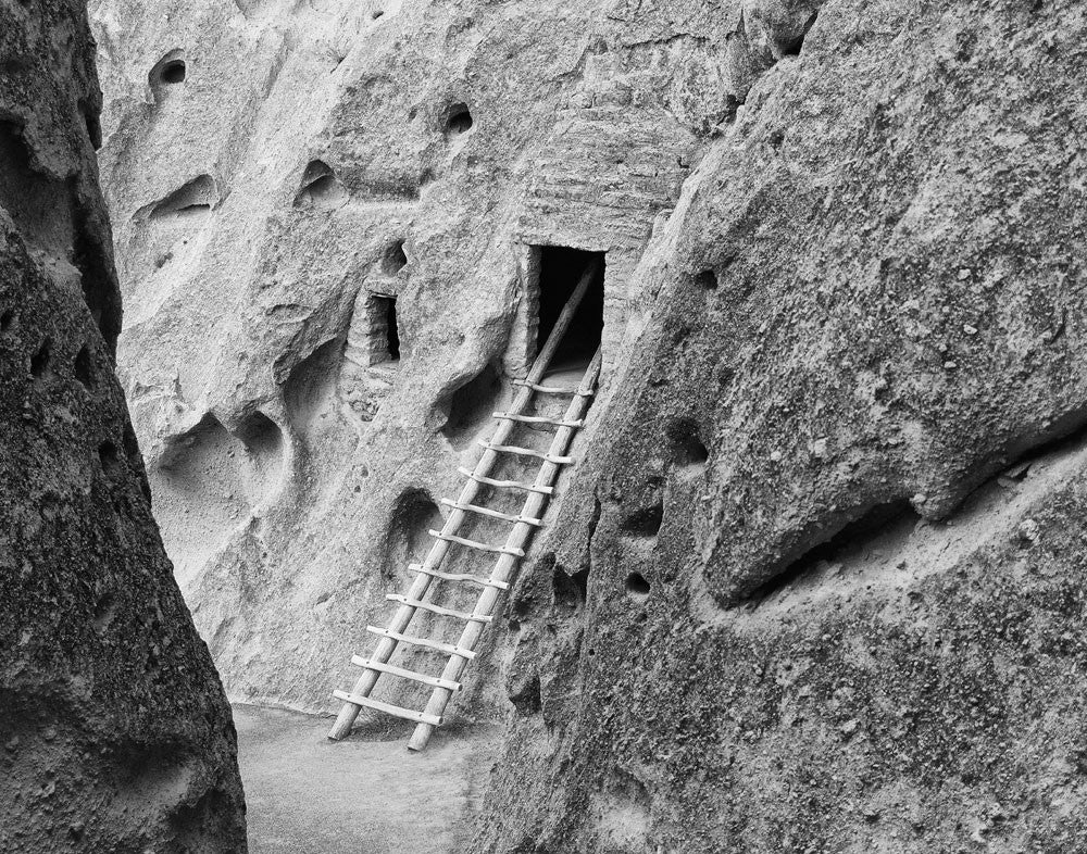 Black and white photograph of a wooden ladder that leads to ancient cliff dwellings at Bandelier National Monument in New Mexico.