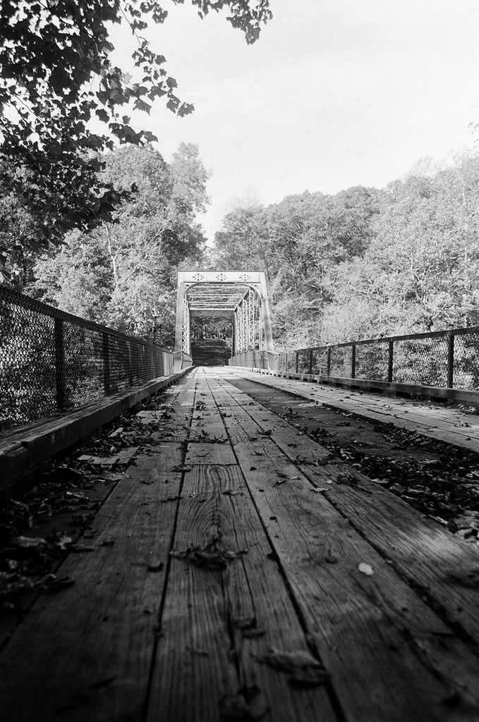 Black and white photograph of an old one-lane bridge with wooden roadbed. This photograph was shot on 35mm Ilford HP5 film, which gives it a grainy look, intrinsic to that brand of film stock.